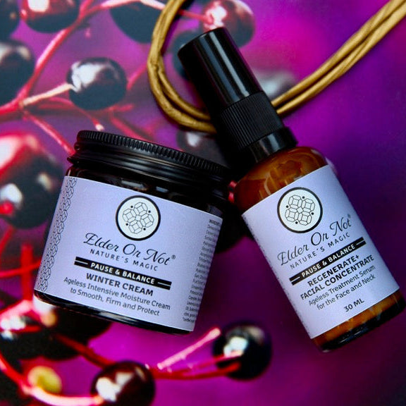 Two skincare products from Elder Or Not Skincare, a jar of Winter Cream and an amber pump bottle of Serum, styled on a purple background with red berries and a kraft paper bag.