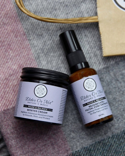 Two skincare products from Elder Or Not Skincare are arranged on a gray and pink plaid blanket alongside a kraft paper shopping bag. The products are an amber jar of face moisturiser and an amber pump bottle of face serum.